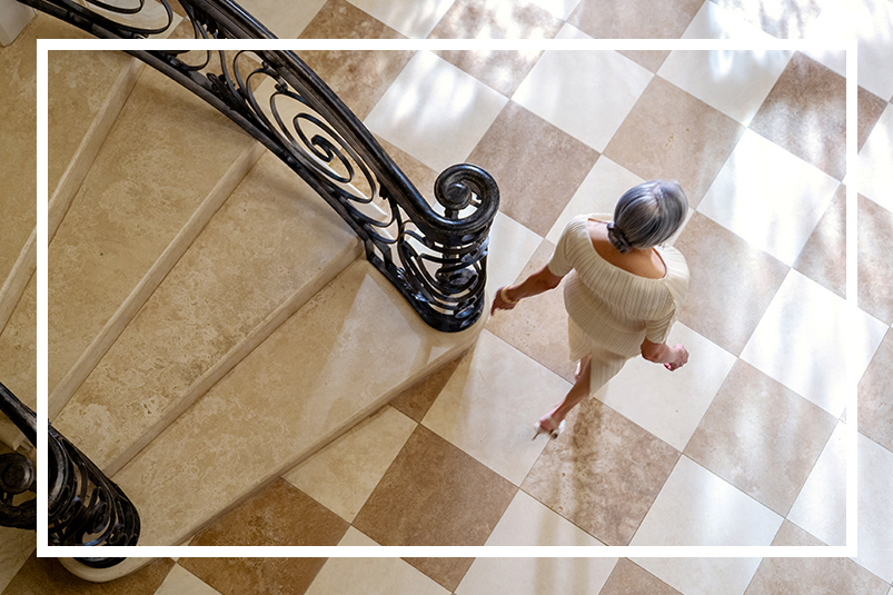 overhead shot of a woman in a white dress walking down the stairs onto a checkered floor